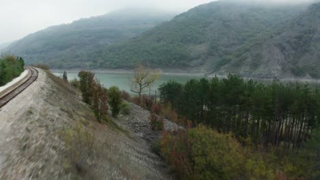 Aerial-view-of-a-lake-surrounded-by-trees,-with-a-fog-covered-mountain-in-the-background