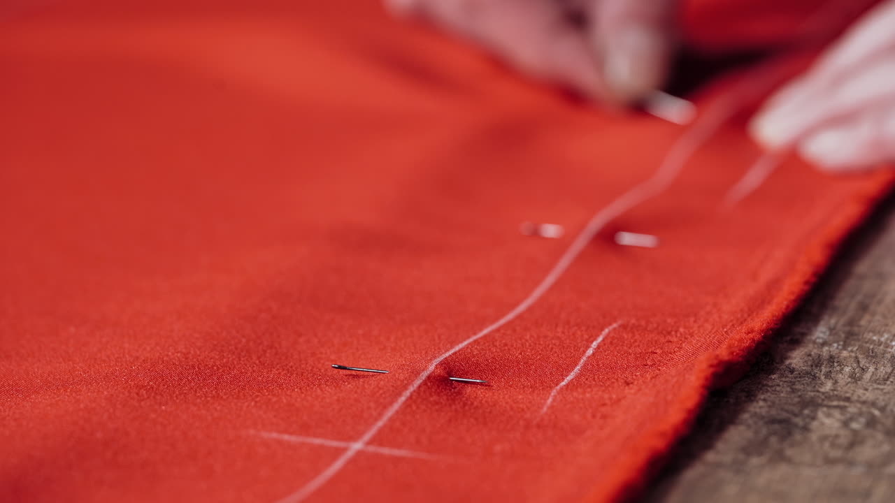 Professional seamstress puts the pins into the red fabric on the table. Woman's hands at work with red cloth and pins in the workshop. Close-up.