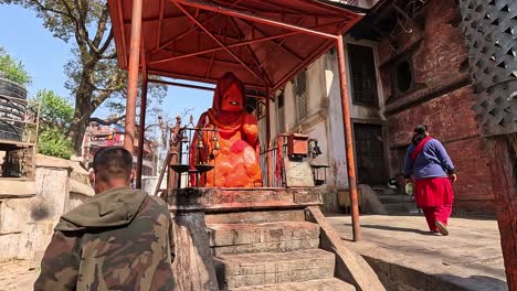faithful devotees gather to pray at the gauri temple pashupatinath, kathmandu.  decorating the hanuman statue covered in vibrant orange. a scene filled with spiritual devotion
