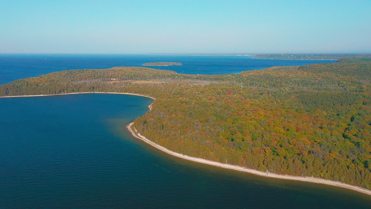 Colorful autumn trees stretch across the Door County peninsula, their warm hues contrasting with the deep blue expanse of Lake Michigan in this tranquil aerial landscape