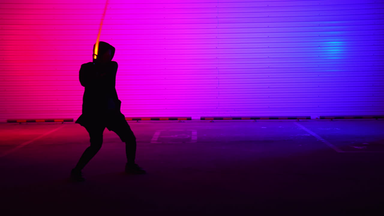 silhouette di una persona che esegue una coreografia d'azione con sabie luminose in un garage con luci colorate