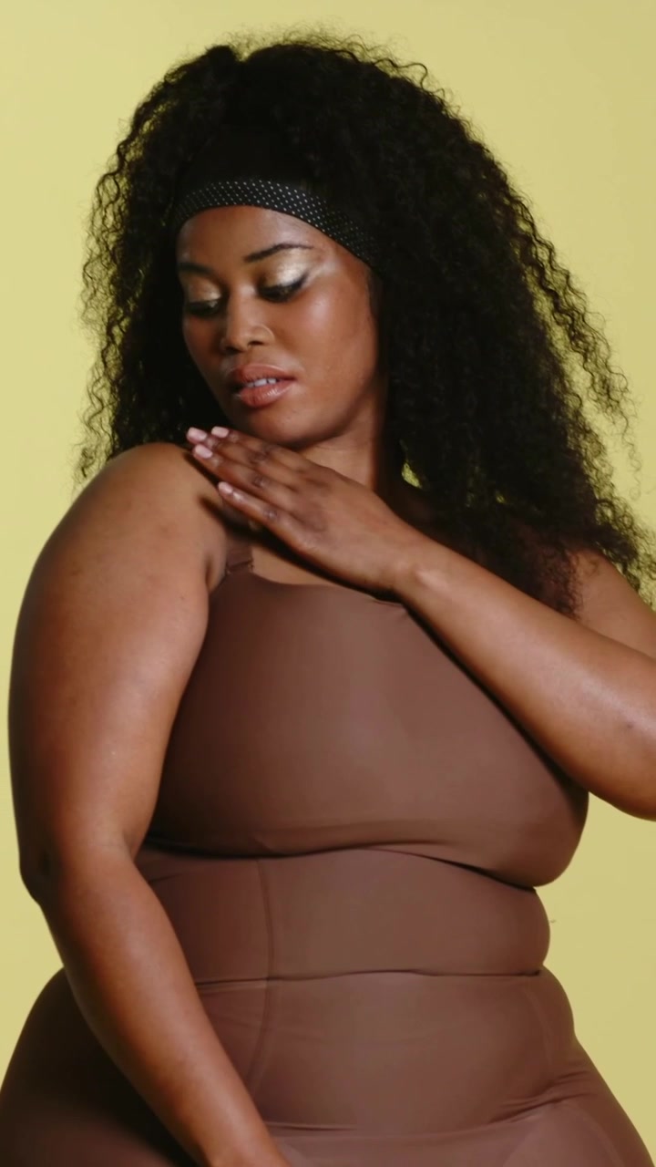Video verticale: Una telecamera che riprende una donna che sistema un intimo modellante marrone, mentre posa su uno sgabello da studio