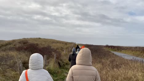 rear view showing group of people walking between dunes during cloudy day in slow motion during cold and windy day