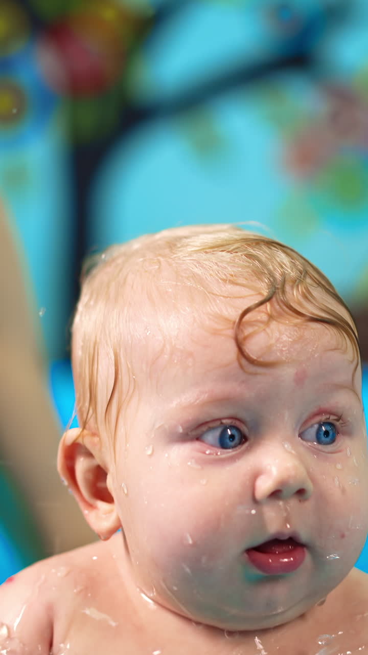 Chubby Caucasian baby is in the swimming pool. Female coach moves the kid in water and he splashes it happily. Vertical video