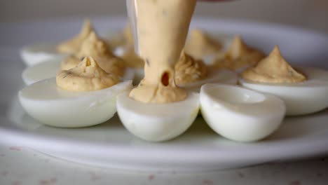 hands of caucasian male filling boiled egg whites with creamy egg yolk mixture using plastic piping bag