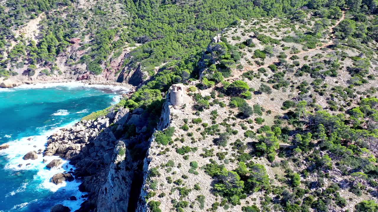 Basset Cove på Mallorca, Spanien, med et tårn, der overser den blå bugt nedenfor, luftfoto med udzoomning, der afslører