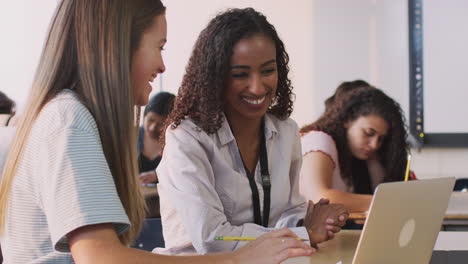 Woman-Teacher-Giving-One-To-One-Support-To-Female-Student-Working-At-Desk-On-Laptop