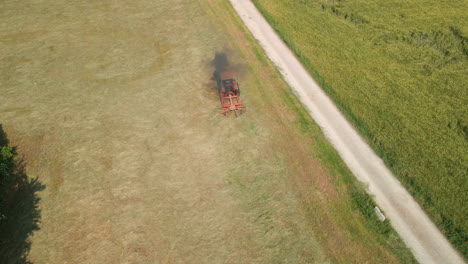 rastrillar heno recién cortado en la granja con rastrillo giratorio tirado por un tractor