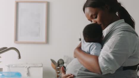 african american mother holding baby working at home washing dishes cleaning kitchen caring for toddler doing housework enjoying motherhood