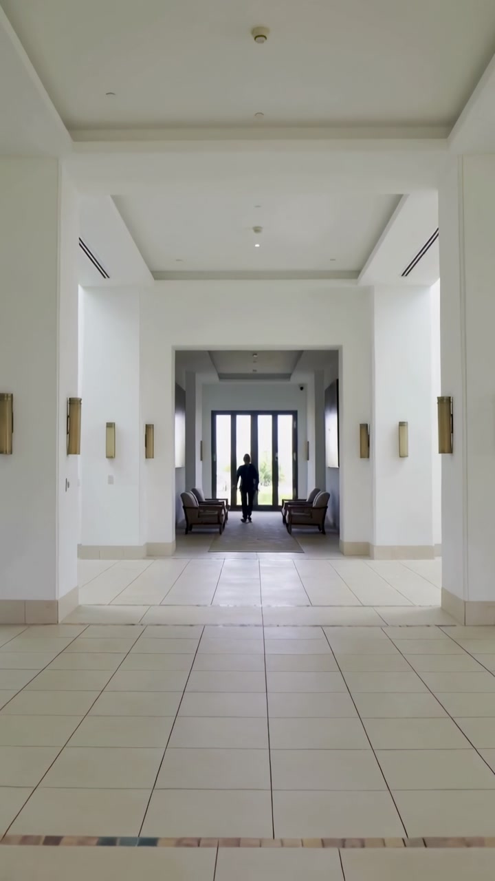 Vertical video: Leaving glass doors, man in dark clothes walking tiled hall approaching camera
