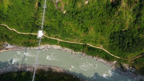 Toma-Aérea-De-Un-Paisaje-Tropical-Con-Río,-Camino-Y-Puente-Colgante-Con-Puenting