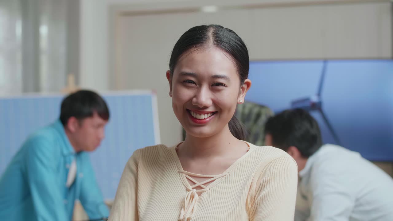 동료들이 사무실에서 풍력 터빈에 대해 논의하는 동안 미소 짓는 아시아 여성 엔지니어가 카메라에 팔을 고 있습니다.