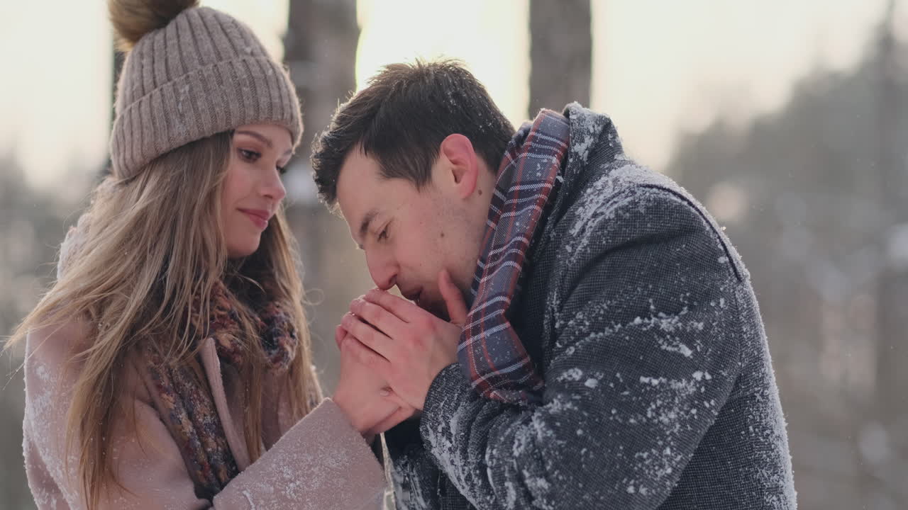 A caring man warms his wife's hands in the winter on the street in a snow-covered Park.