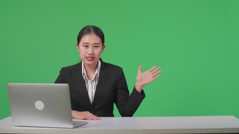 Live News Studio With Professional Asian Female Anchor And Her Computer Pointing On Something While Reporting On The Events Of The Day On The Green Screen