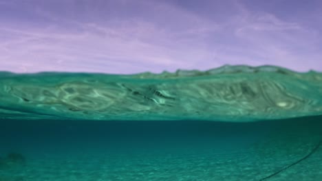 half under water view of sailing ship moored at horizon and clear transparent seawater with coast in background