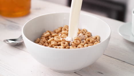 preparar el desayuno: verter leche en un cuenco de cereales integrales crujientes colocados en una mesa de la cocina, en cámara lenta