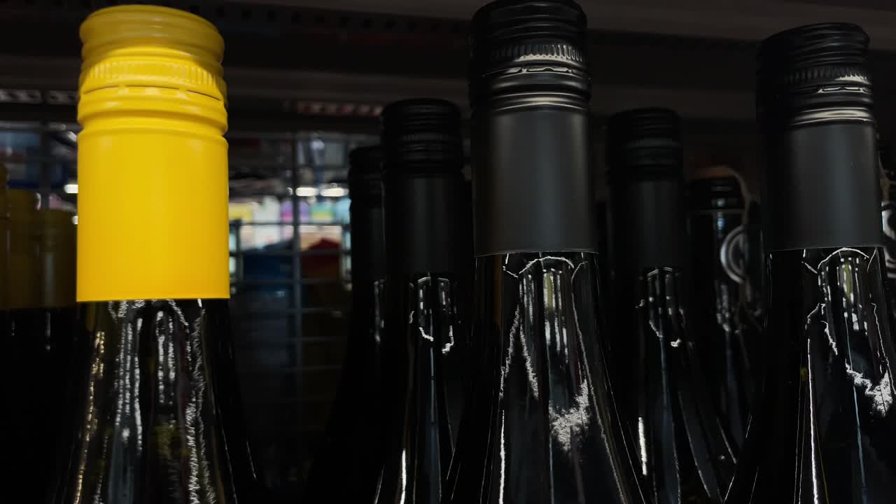 Alcohol wine bottles in a row on store shelf lined up, close up of neck and top