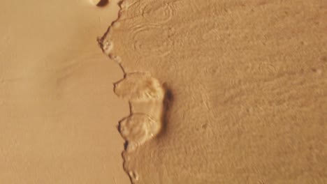 A-slow-motion-shot-following-footprints-just-at-the-shore-of-the-beach