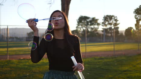 hermosa mujer hispana soplando burbujas de ensueño mientras sonríe y se ve juguetona al aire libre al atardecer