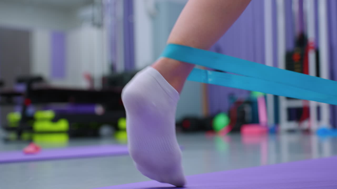 vista de cerca de la pierna de una persona que se estira con una banda de resistencia, equipo de gimnasia ligeramente borroso en el fondo, haciendo hincapié en la aptitud y el entrenamiento de fuerza