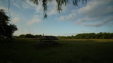 Time-lapse-clouds-over-green-pasture-at-sunrise-with-boat-and-canoe-storage-in-foreground