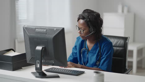 mujer negra médico usar bata blanca gafas y auriculares hablando con el cliente uso de videollamada. debido al brote de la pandemia de coronavirus terapeuta trabajando de forma remota proporcionar ayuda a los pacientes de la clínica por videollamada