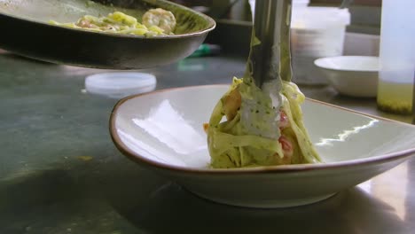 el chef coloca pasta de salsa blanca de mariscos en un plato con pinzas