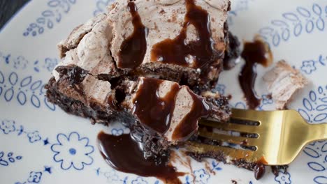 fork taking bite out of baked brownie dessert slice topped with meringue and drizzled chocolate syrup