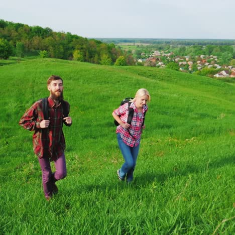 A-Couple-Of-Tourists-With-Backpacks-Are-Walking-Along-The-Crest-Of-A-Large-Green-Hill-7
