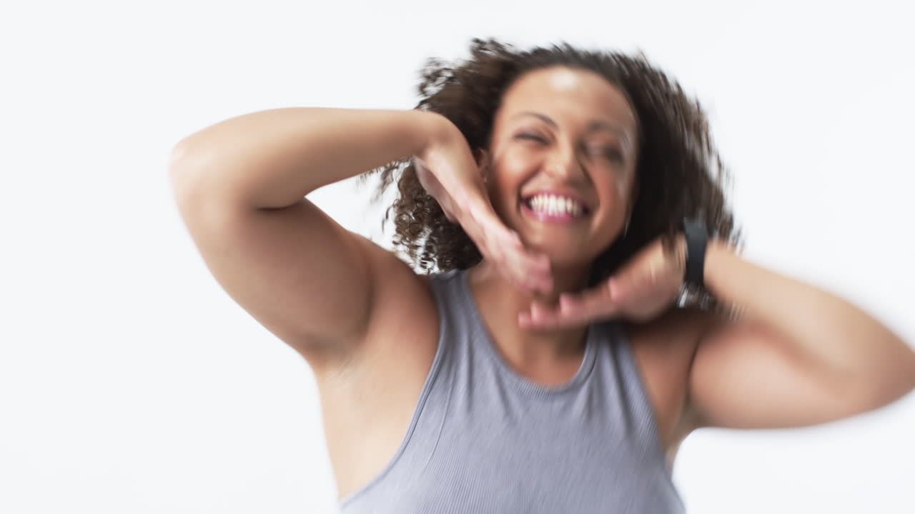 Young biracial plus size woman with curly hair smiling and posing with hands under chin