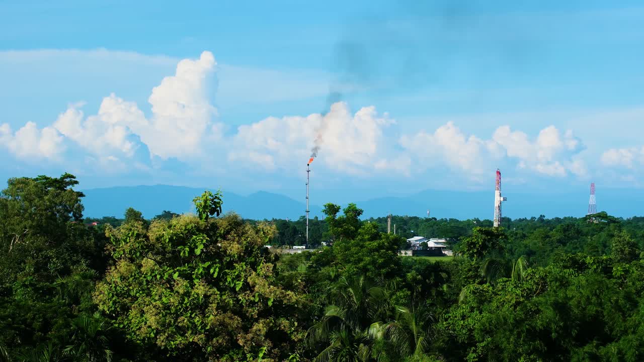 가스 필드 굴은 구름과 파란 하늘과 함께 울창한 녹색 숲 근처의 연기로 공기를 오염시니다.