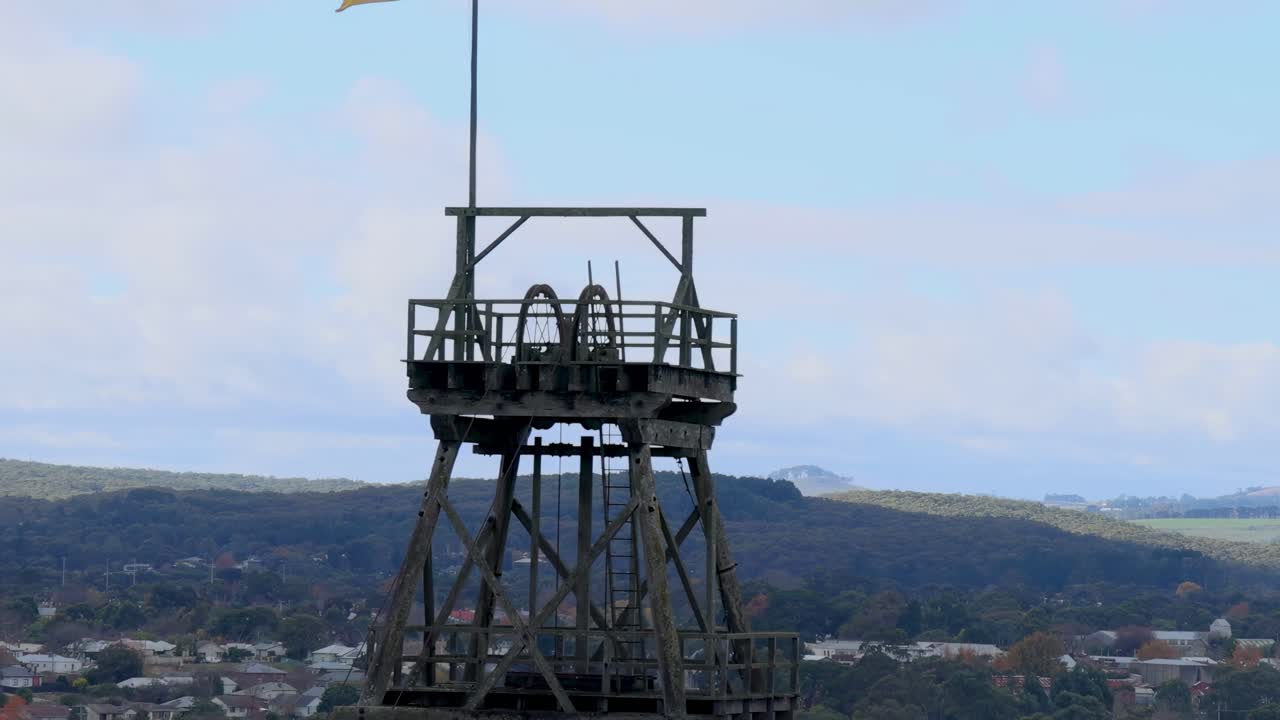 A wooden observation tower stands against a backdrop of rolling hills and a partly cloudy sky.