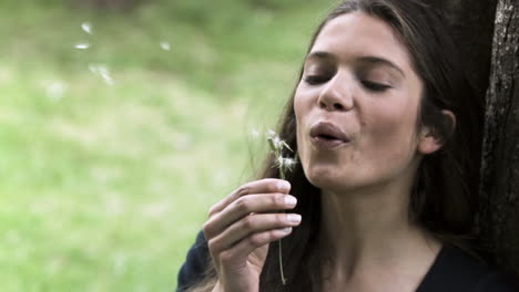 relaxed woman in slow motion blowing a dandelion