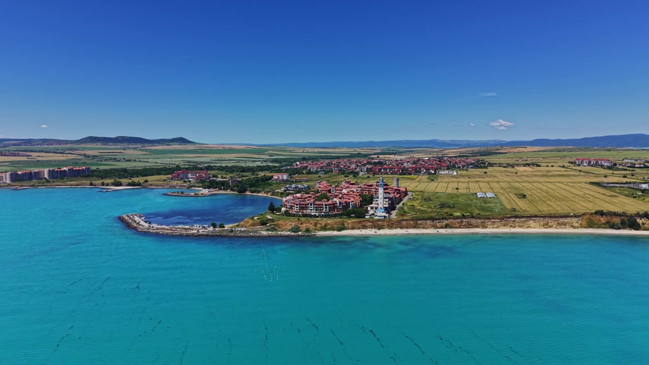 Yazın öğle vakti bir kıyı tatil köyü ve mavi sular manzarası.