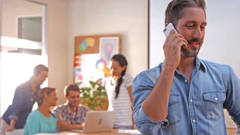 Casual-businessman-having-phone-call-with-his-colleagues-behind-him