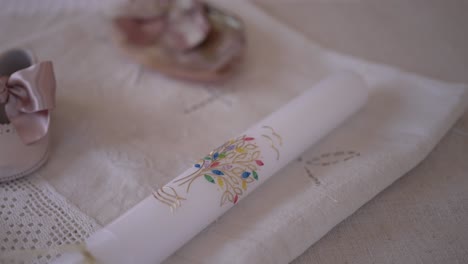 decorative christening candle with floral design, paired with baby shoes and a seashell, placed on a lace covered cloth, symbolizing a sacred ceremony