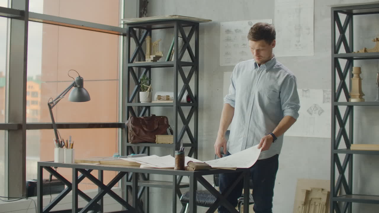 el ingeniero trabaja en una oficina luminosa con una gran ventana se concentra y dibuja planos. lugar de trabajo de un arquitecto o diseñador: estilo loft dibujos interiores minimalistas y café en la mesa.