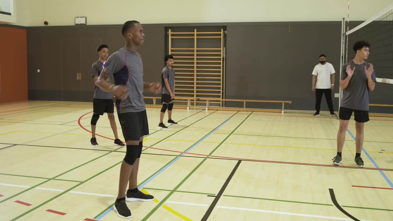 Des joueurs de volleyball masculins diversifiés s'entraînant à la réception de service dans un gymnase, l'entraîneur leur lançant le ballon.
