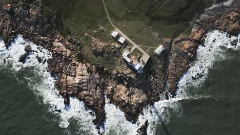 Aerial-view-looking-down-at-waves-crashing-against-Cabo-Polonio-green-lush-coastline,-Uruguay