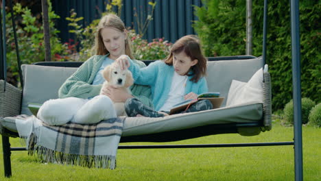 two girlfriends are relaxing in the garden at the backyard of the house, playing with a cute puppy. sitting on a garden swing