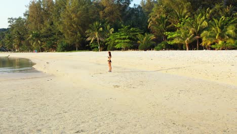 girl standing on white sandy beach washed by calm clear water of shallow lagoon reflecting palm trees in vietnam