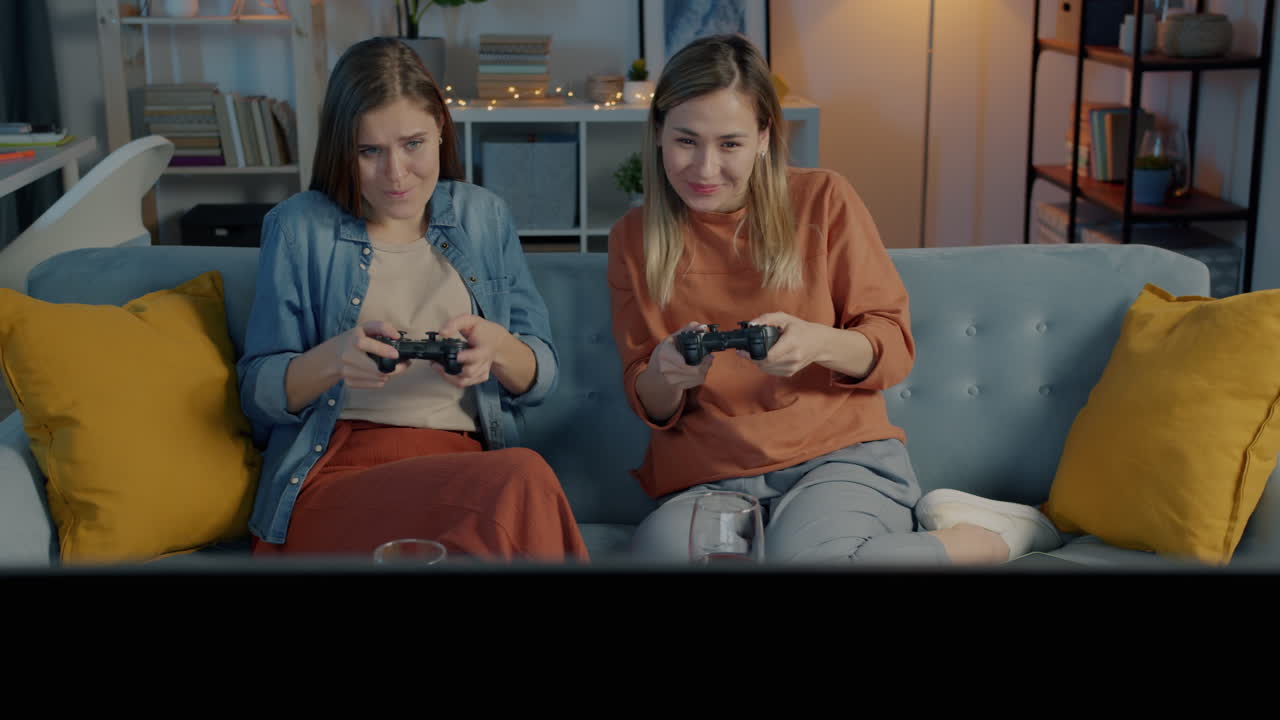 Due donne che giocano ai videogiochi su un divano di notte