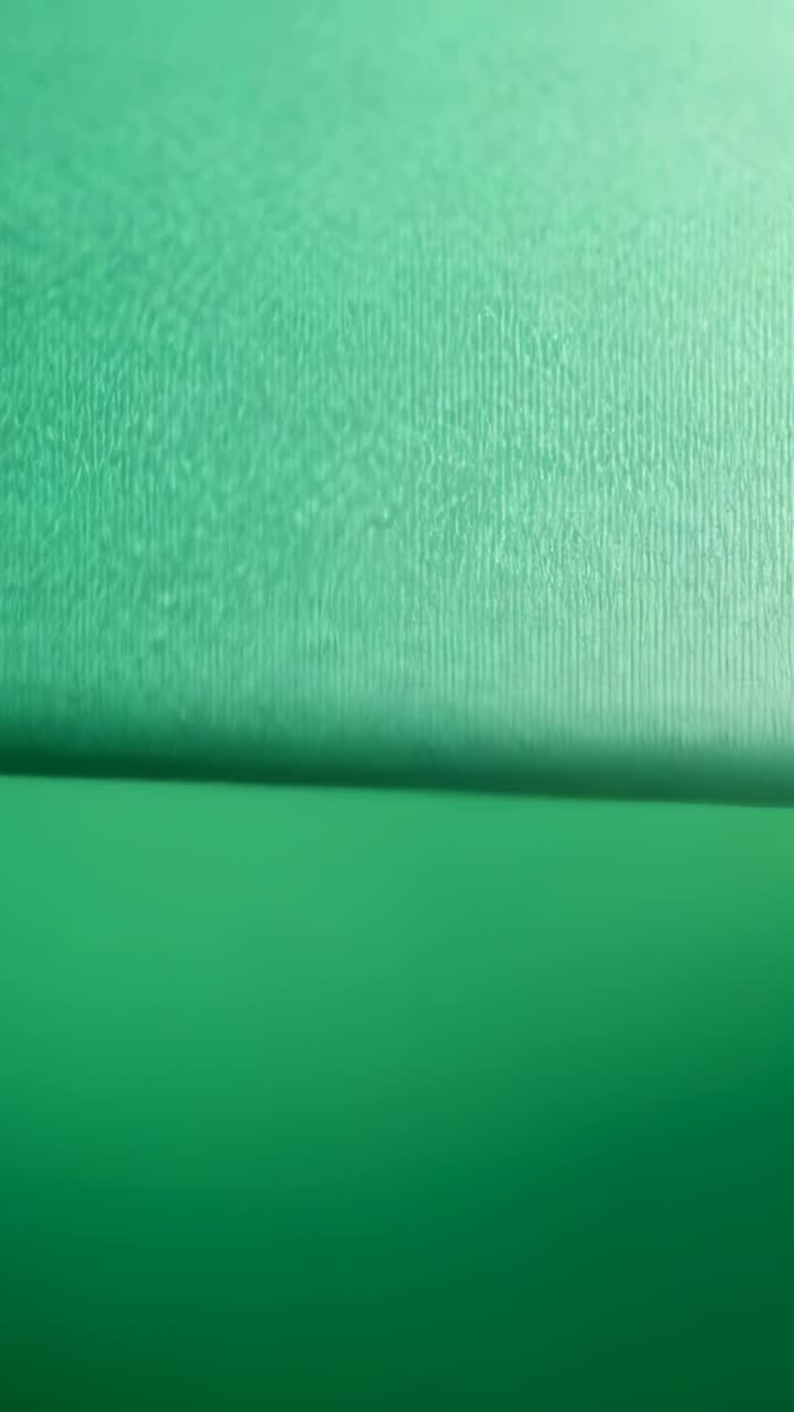 Vídeo vertical: Câmera se aproximando, revelando superfície verde texturizada no estúdio, com a costura subindo.