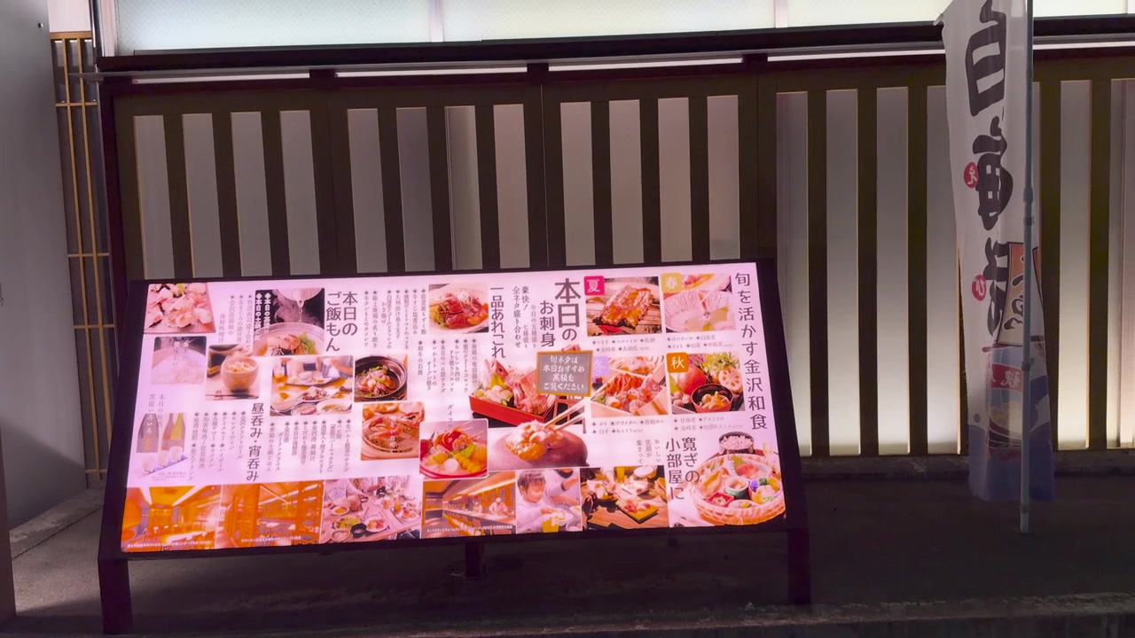Et glødende utendørs menytavle viser sjømatretter utenfor en tradisjonell restaurant i Kanazawa, Japan.
