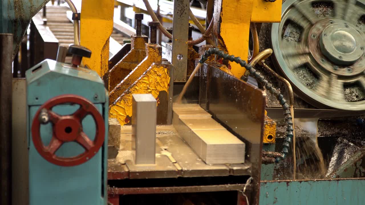 Sierra de cinta industrial, cortando aluminio metálico, refrigerante en escena amarilla, herramientas industriales
