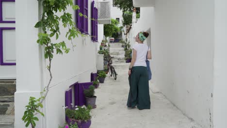 una mujer caminando en una calle blanca estrecha con ventanas púrpuras