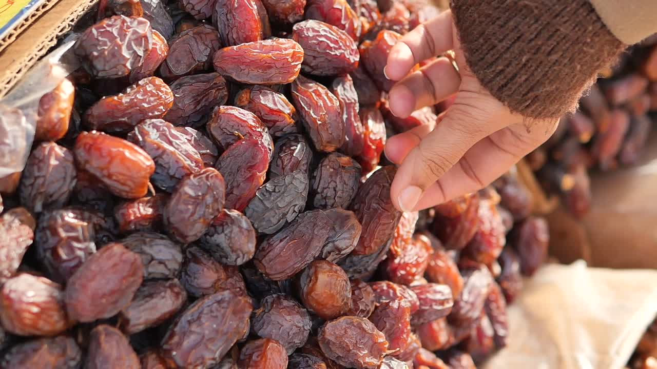 Close-up of Hand Selecting Fresh Dates from a Pile at a Market
