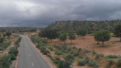 Tiro-Aéreo-Ascendente-Sobre-La-Carretera-Remota-A-Través-De-Tharparkar-En-Sindh-Con-Nubes-De-Mal-Humor-Cubiertas