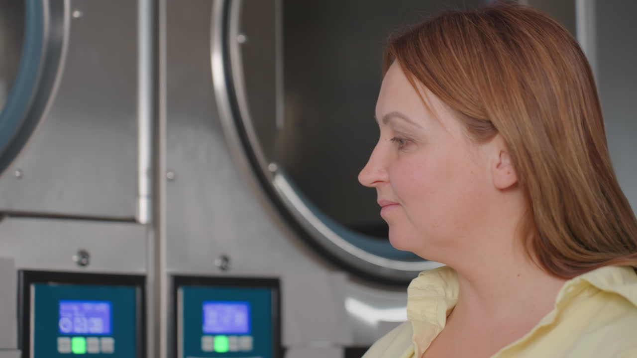 Side profile professional inspects dryer system as machines run in laundromat, confirming safe operation, service quality, cleanliness, reliability, customer care standard, digital panels glowing