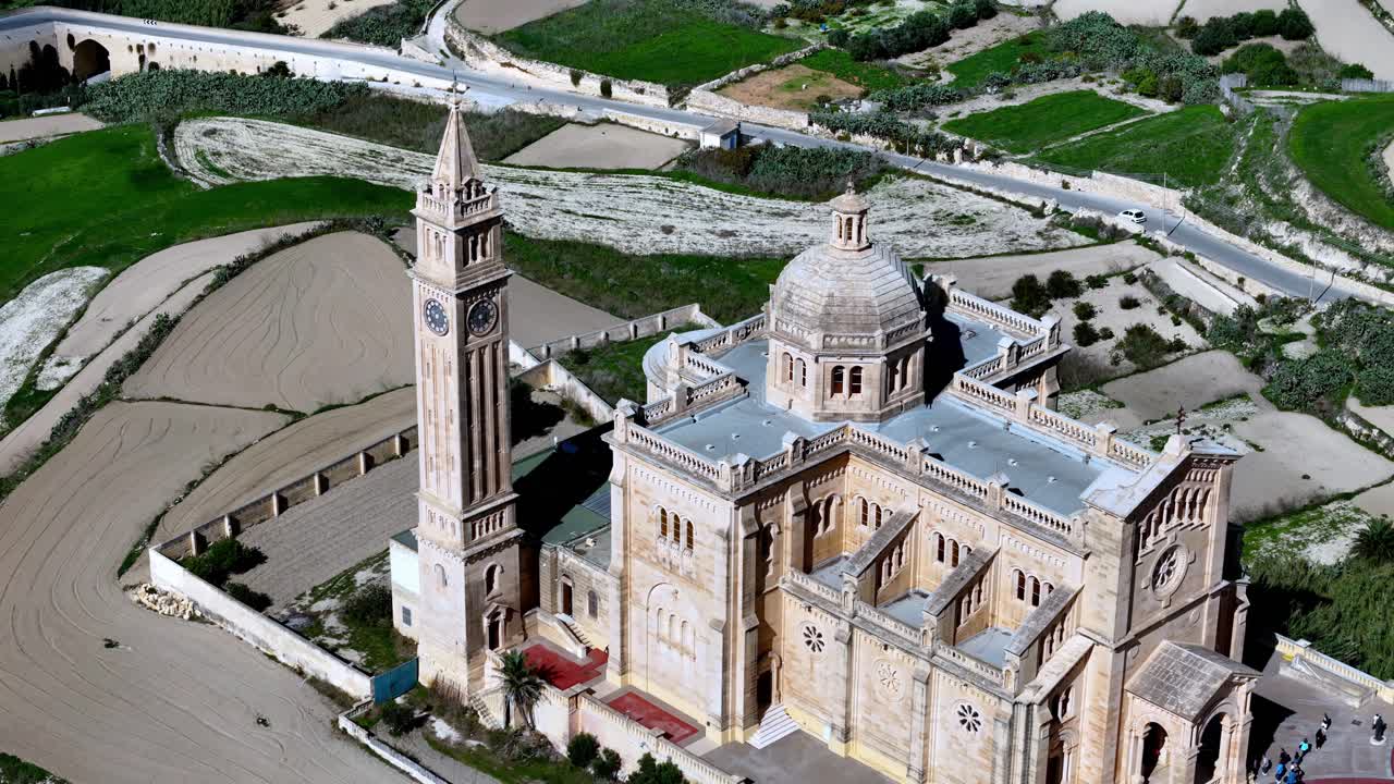Huzurlu bir bahar gününde, parlak Akdeniz güneşi altında, altın rengi kireçtaşı ve yeşil tarlalarla çevrili Malta'nın Gozo Adası'ndaki görkemli Ta Pinu Ulusal Tapınağı'nın yüksekten havadan çekilmiş görüntüsü.